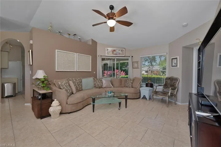 Living area with arched walkways, light tile patterned floors, lofted ceiling, and a ceiling fan