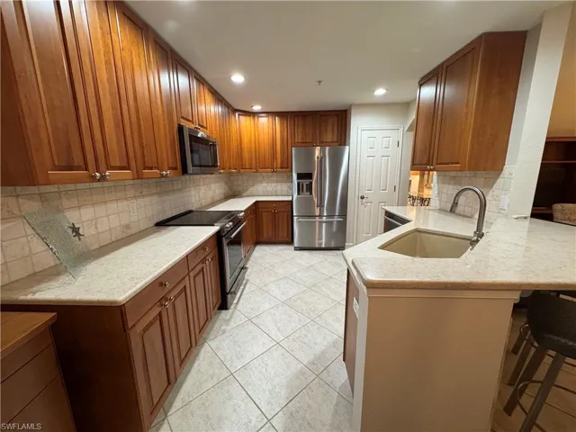 Kitchen featuring stainless steel appliances, cherry wood cabinets, light quartz countertops, and recessed lighting