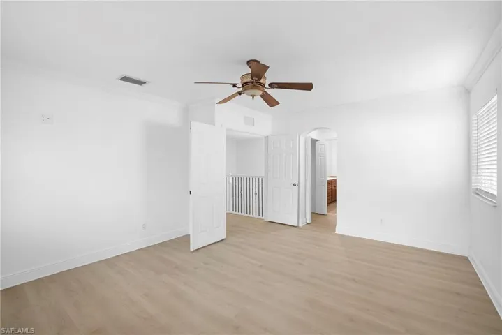 Bedroom featuring crown molding, light wood-type flooring, arched walkways, and ceiling fan