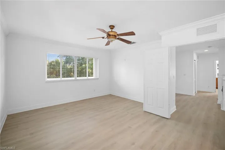 Primary bedroom room with light wood-style floors, ornamental molding, and a ceiling fan