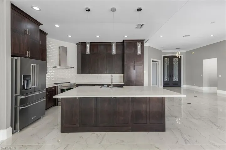 Kitchen featuring wall chimney exhaust hood, an island with sink, stainless steel appliances, ornamental molding, and sink