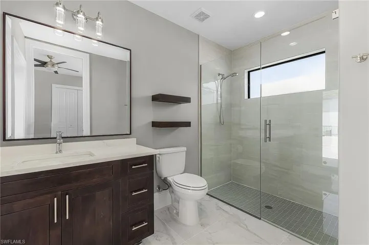Bathroom featuring a shower with shower door, ceiling fan, toilet, and vanity