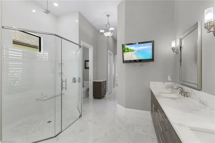 Bathroom with toilet, a shower with door, an inviting chandelier, and vanity