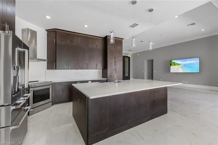 Kitchen with a kitchen island with sink, pendant lighting, stainless steel appliances, sink, and wall chimney range hood