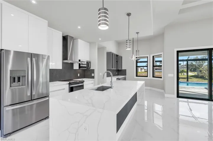 Kitchen with pendant lighting, stainless steel appliances, a center island with sink, and wall chimney range hood