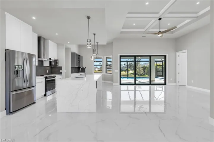 Kitchen with wall chimney exhaust hood, coffered ceiling, sink, stainless steel appliances, and a kitchen island with sink