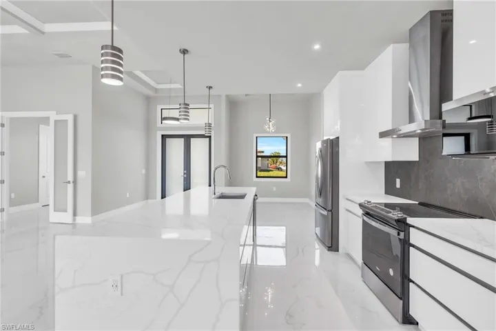 Kitchen with wall chimney exhaust hood, white cabinetry, light stone counters, decorative light fixtures, and appliances with stainless steel finishes
