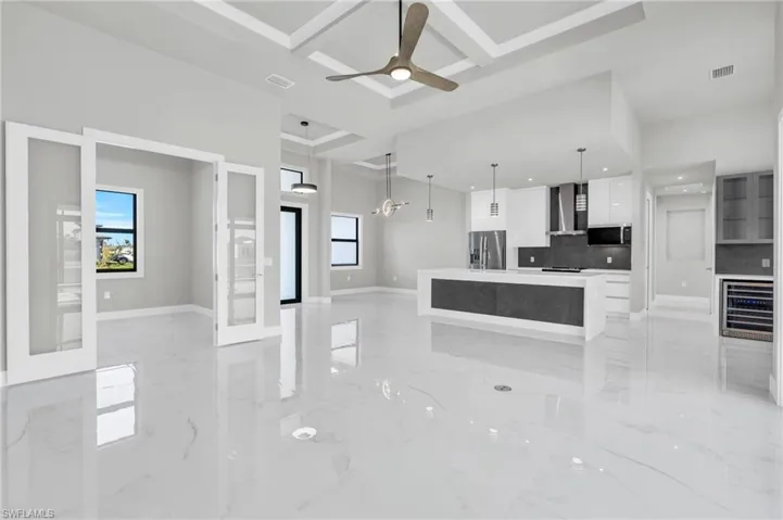 Kitchen with coffered ceiling, a center island, stainless steel fridge with ice dispenser, wall chimney range hood, and white cabinets