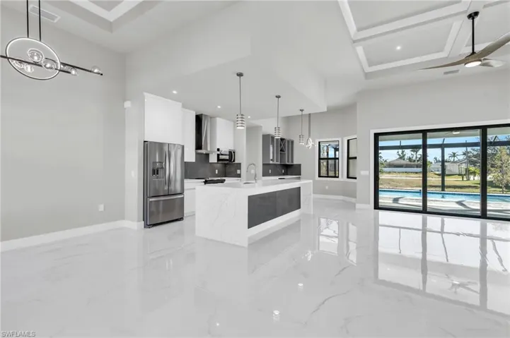 Kitchen featuring pendant lighting, stainless steel appliances, light stone counters, an island with sink, and white cabinets