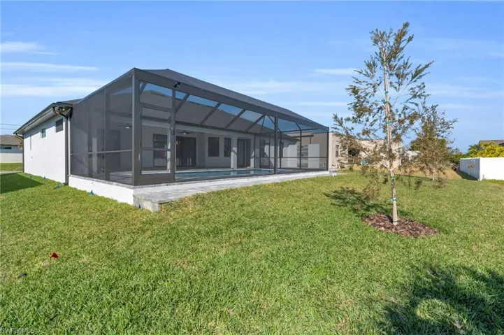 Rear view of house with glass enclosure and a lawn