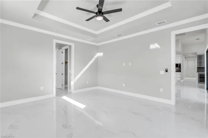 Empty room with a raised ceiling, crown molding, and ceiling fan