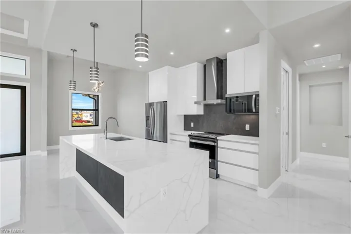Kitchen with appliances with stainless steel finishes, white cabinetry, an island with sink, sink, and wall chimney range hood