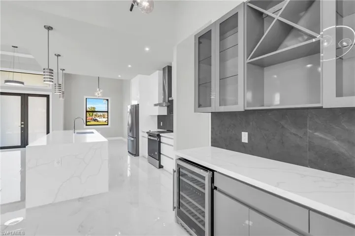 Kitchen featuring pendant lighting, wine cooler, light stone counters, stainless steel appliances, and wall chimney range hood