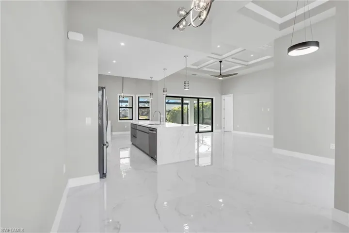 Kitchen featuring appliances with stainless steel finishes, a spacious island, coffered ceiling, light stone counters, and decorative light fixtures
