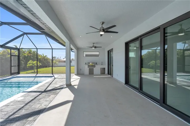 View of pool with exterior kitchen, a patio, ceiling fan, and glass enclosure