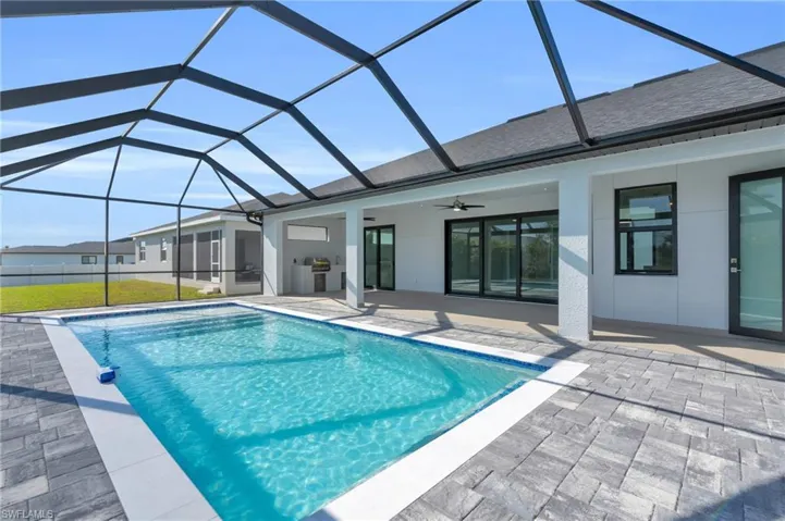 View of swimming pool with a grill, a patio area, ceiling fan, and glass enclosure
