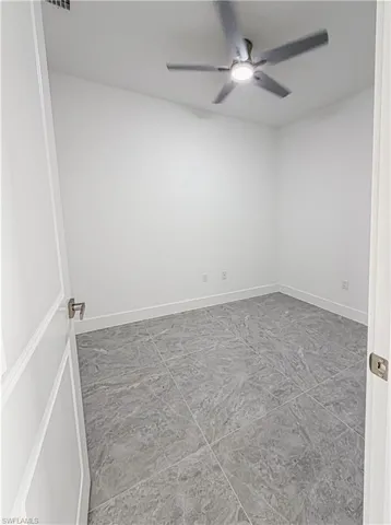 Modern room featuring large format grey floor tiles, white walls, and a ceiling fan with integrated lighting