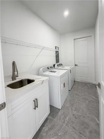 Laundry room featuring a utility sink with a brushed metal faucet, white cabinetry, and a stone-finish countertop