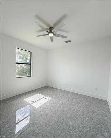Bright room featuring polished gray tile flooring, a modern ceiling fan with integrated lighting, a recessed ceiling light, a single-pane window with black trim, and crisp white baseboards
