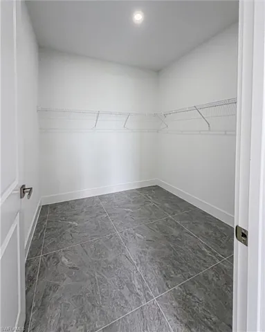 Walk-in storage space featuring grey large-format tile flooring, white wire shelving, a recessed ceiling light, and white baseboards