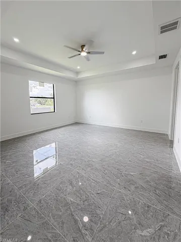 Spacious room featuring large format grey tile flooring, a tray ceiling with recessed lighting, and a modern ceiling fan