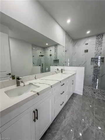 Spacious bathroom featuring a dual vanity with white cabinetry and patterned countertops, undermount sinks, and dark bronze fixtures