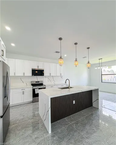 Bright kitchen featuring a waterfall island with a fluted wood-finish accent panel, quartz countertops and backsplash, integrated sink with a gooseneck faucet, and white shaker-style cabinetry