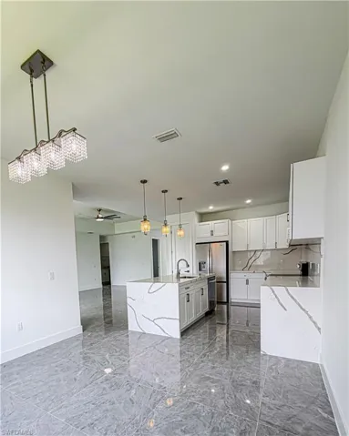 Contemporary kitchen featuring a waterfall island, white cabinetry, integrated stainless steel appliances, pendant lighting, and polished stone tile flooring