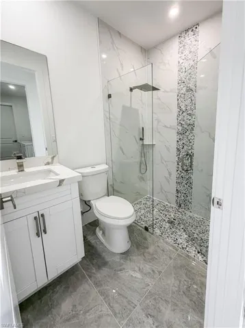 Contemporary bathroom featuring a frameless glass shower enclosure, a rain showerhead, a pebble-tiled shower floor, and a full-height marble-look tiled shower surround with a decorative mosaic accent