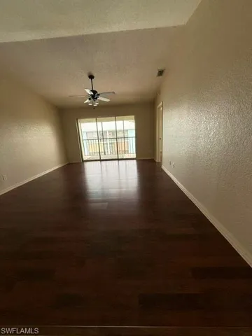 Spacious interior featuring dark wood-finish flooring, light-toned textured walls, and a ceiling fan with integrated lighting