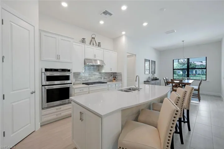 Kitchen with an island with sink, hanging light fixtures, stainless steel appliances, sink, and white cabinets