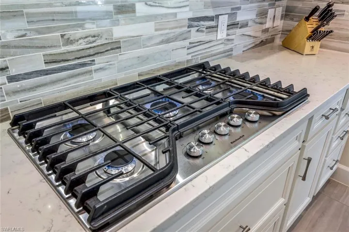 Exterior details with white cabinets, light stone countertops, decorative backsplash, and stainless steel gas stovetop
