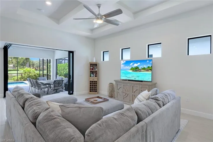 Living room featuring coffered ceiling, ceiling fan, and a wealth of natural light