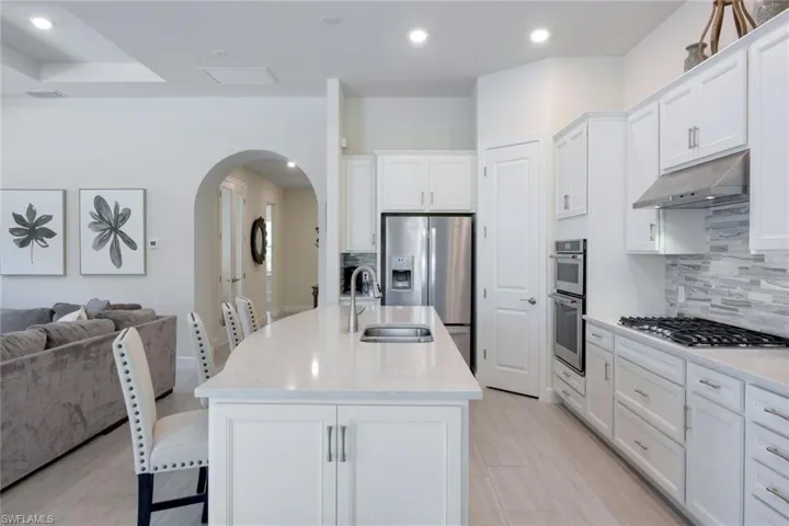 Kitchen featuring light stone countertops, appliances with stainless steel finishes, backsplash, an island with sink, and white cabinets