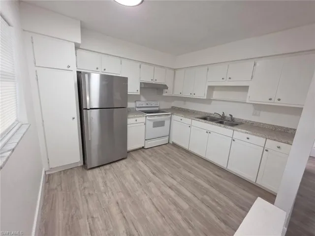 Kitchen featuring freestanding refrigerator, white electric range, white cabinets, light wood-type flooring, and light countertops