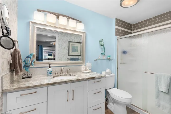 Bathroom featuring backsplash, vanity, walk in shower, ceiling fan, and toilet