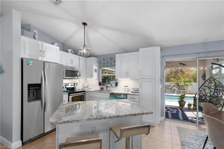 Kitchen with white cabinetry, hanging light fixtures, stainless steel appliances, a center island, and sink