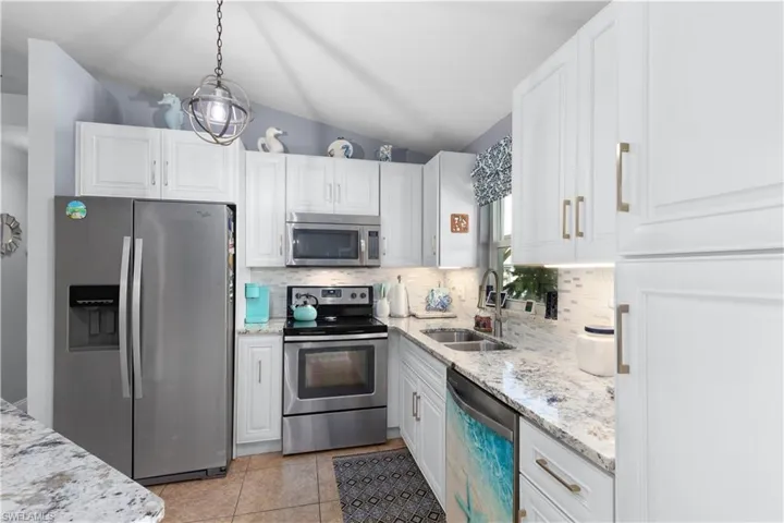 Kitchen featuring stainless steel appliances, hanging light fixtures, sink, white cabinets, and decorative backsplash
