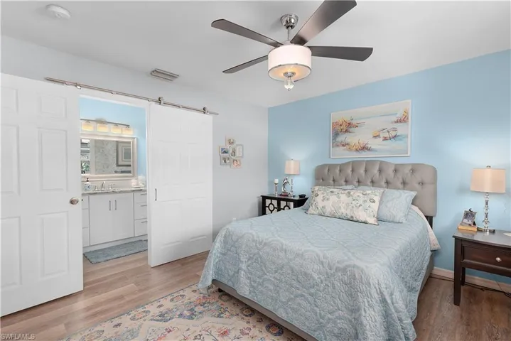 Bedroom featuring sink, ceiling fan, light hardwood / wood-style floors, and a barn door