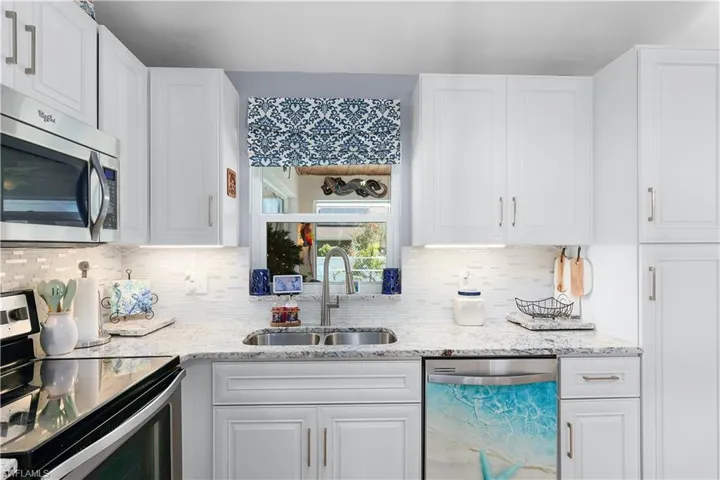 Kitchen with white cabinetry, stainless steel appliances, backsplash, and sink