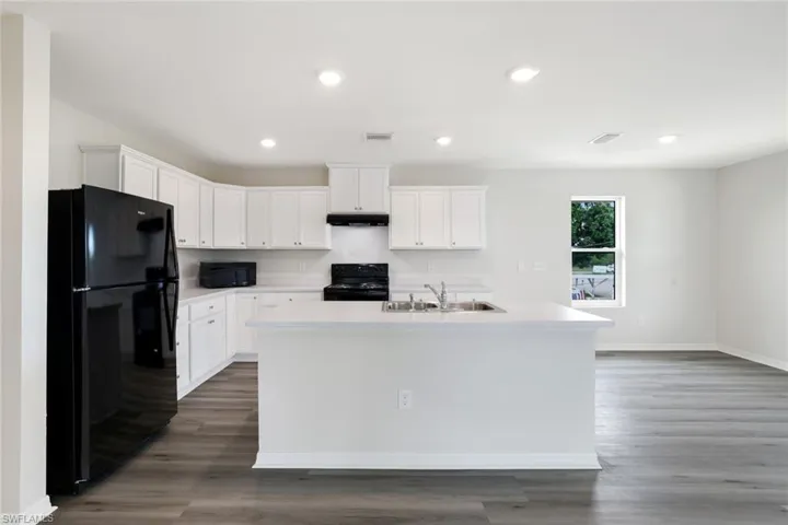 Kitchen with black appliances, wood finished floors, white cabinetry, light countertops, and recessed lighting