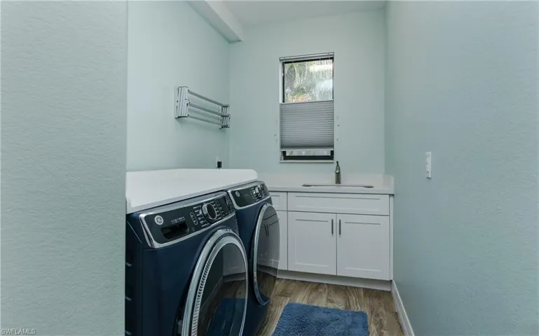 Laundry room featuring a textured wall, washing machine and dryer, light wood-style flooring, and cabinet space