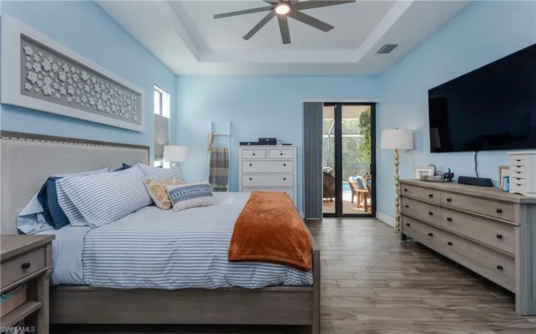 Bedroom with multiple windows, access to exterior, light wood-style floors, a ceiling fan, and a tray ceiling