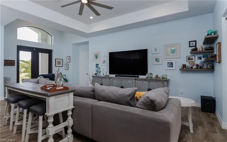 Living area featuring wood finished floors, a ceiling fan, a high tray ceiling, and french doors