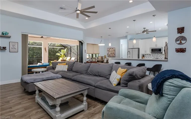 Living area with a sunroom, ceiling fan, light wood-style floors, a tray ceiling, and recessed lighting