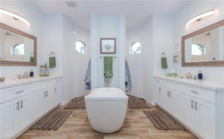 Bathroom with walk in shower, two vanities, light wood-type flooring, and a soaking tub