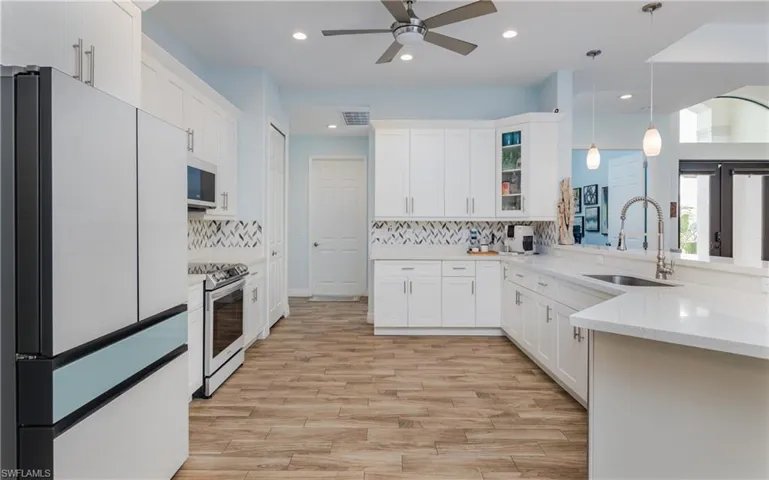 Kitchen with freestanding refrigerator, white cabinets, glass fronted cabinets, hanging light fixtures, and light wood-style flooring