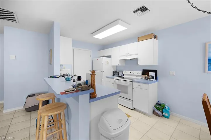 Kitchen with a breakfast bar, white appliances, white cabinets, a peninsula, and light tile patterned floors