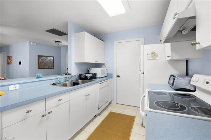 Kitchen with white cabinets, white appliances, light countertops, and light tile patterned flooring