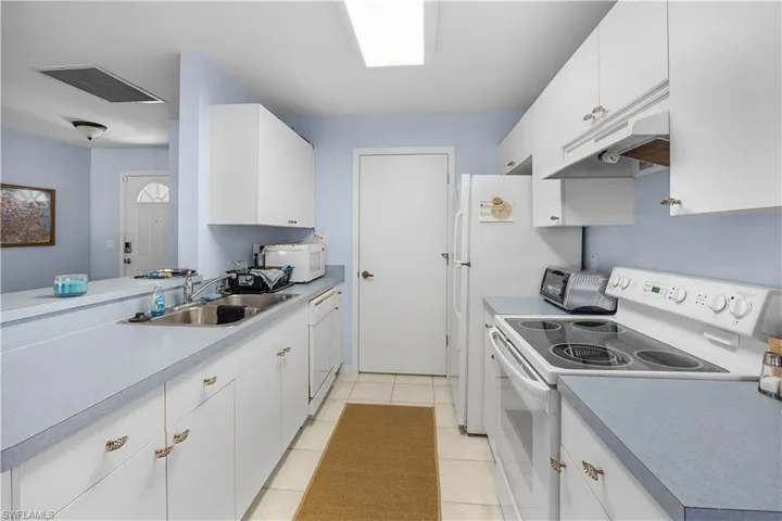Kitchen featuring white cabinetry, white appliances, light tile patterned flooring, and light countertops